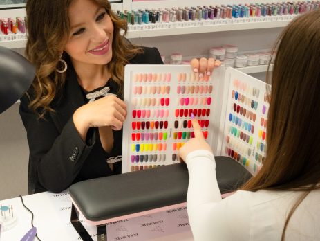 Prothésiste ongulaire en train de réaliser une pose sur une cliente fidèle dans un institut moderne et chaleureux.