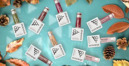 Fond vert décoré de flacons de vernis semi-permanent aux couleurs tendance de l’automne (orange brûlé, bordeaux, marron, nude, vert sapin). Des feuilles d’automne dispersées complètent la scène pour rappeler la saison et mettre en valeur les teintes.